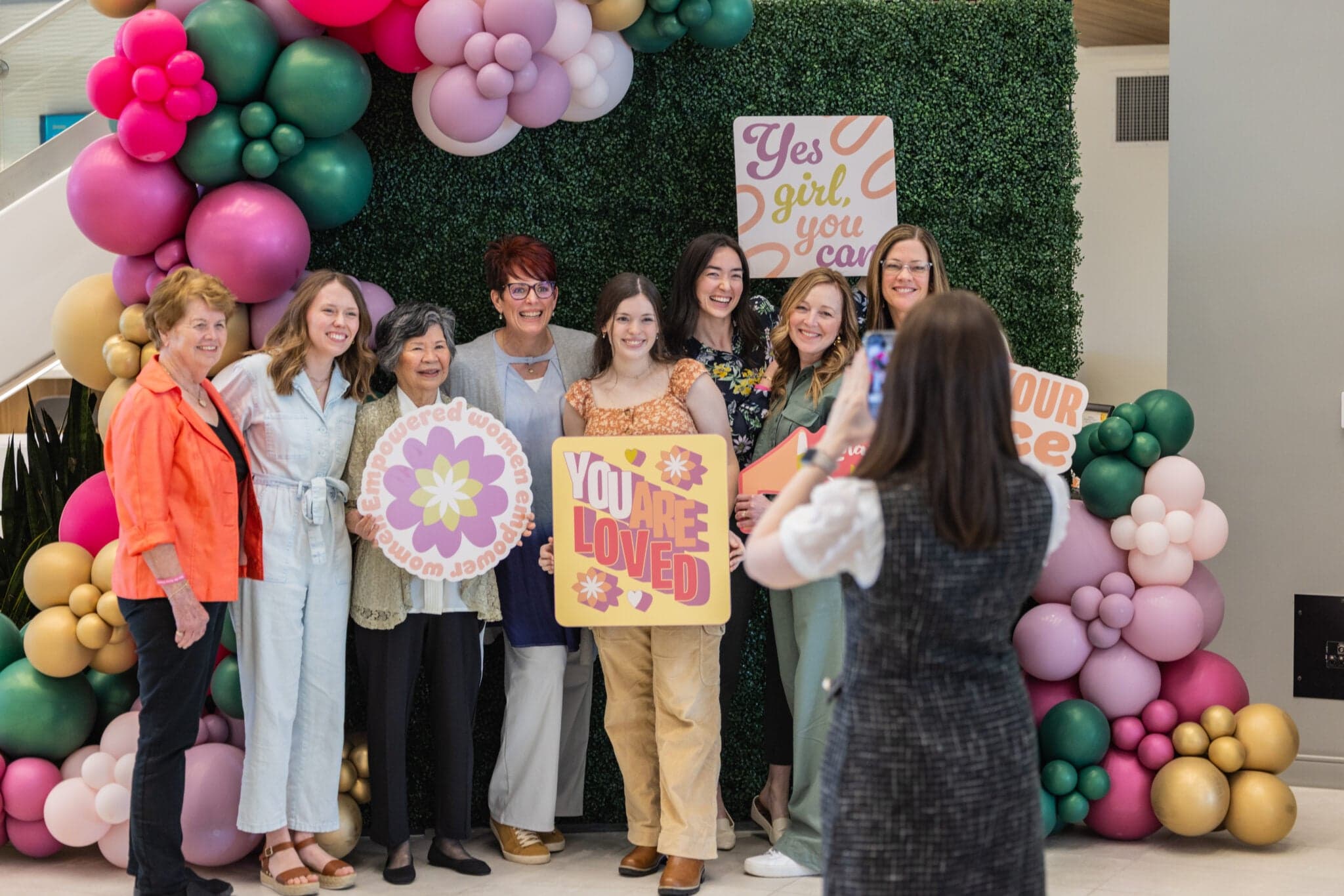 Guests posing with signs at a balloon-framed photo backdrop