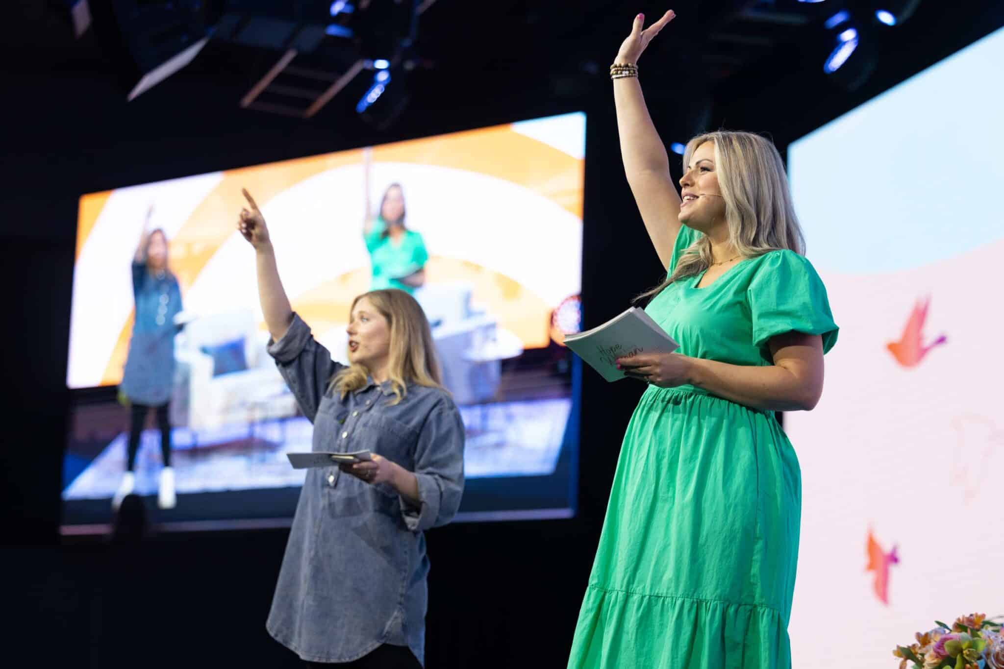 Two hosts waving to the audience from the stage